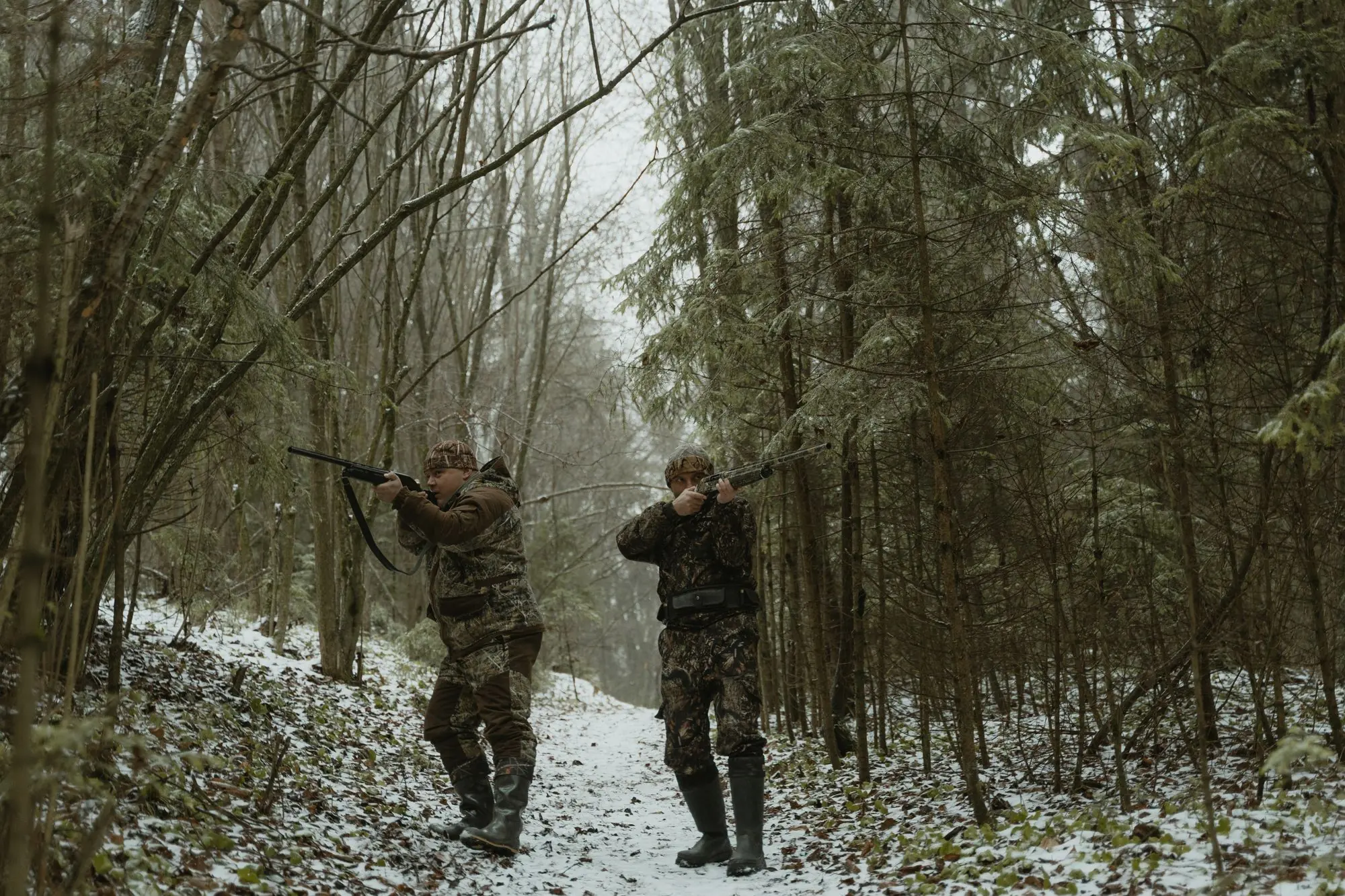 Two hunters in camouflage walking through a snowy forest